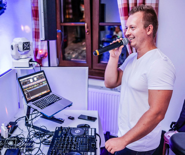Pavel Kříž s mikrofonem u DJ pultu během akce.